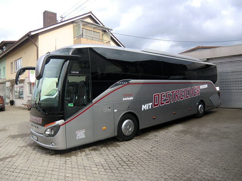 Ein silberner Bus mit der Aufschrift „Oestreicher“ an der Seite steht vor einem Gebäude.