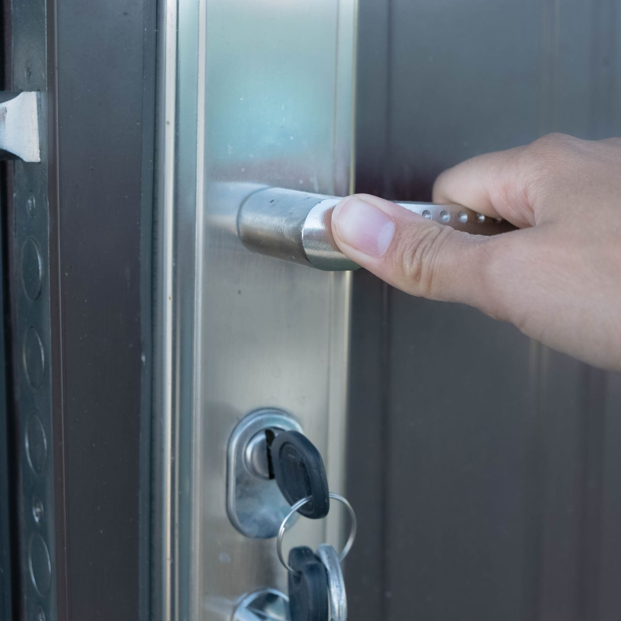 Main ouvrant une poignée de porte en argent avec des clés dans la serrure.