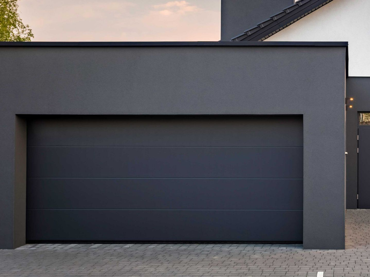 Porte de garage grise sur une maison moderne avec un extérieur sombre assorti et une petite porte à droite.