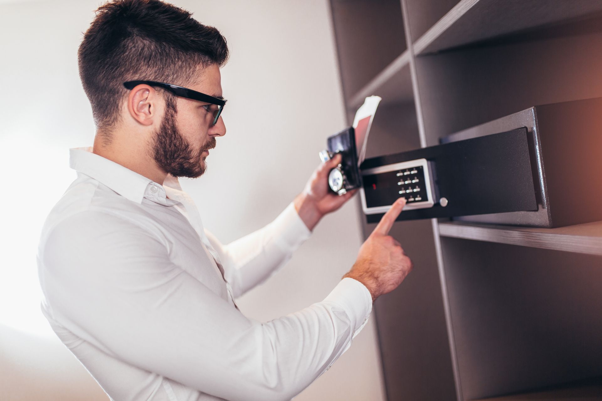 Un homme en chemise blanche ouvre un coffre-fort numérique dans une étagère en bois.