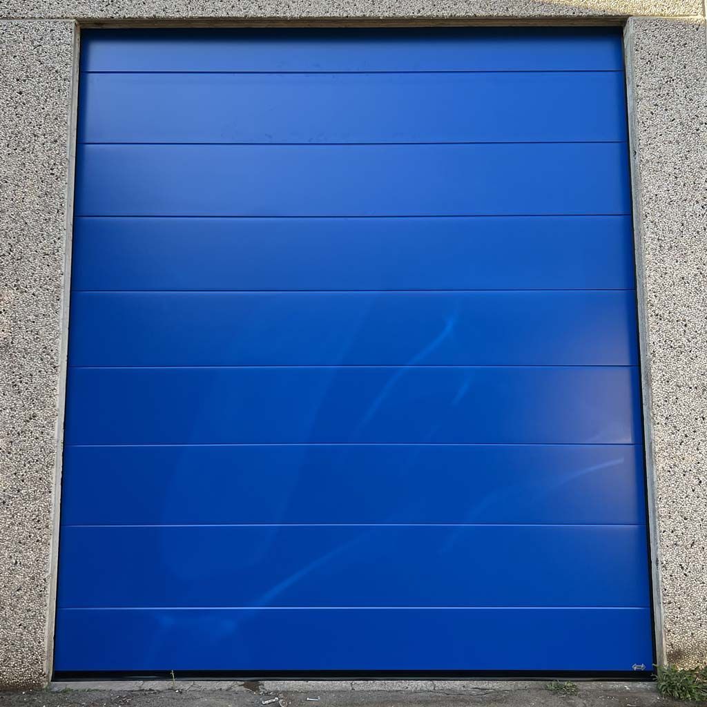 Portes de sécurité grises, fermées et enroulables sur un bâtiment commercial, partiellement visibles.