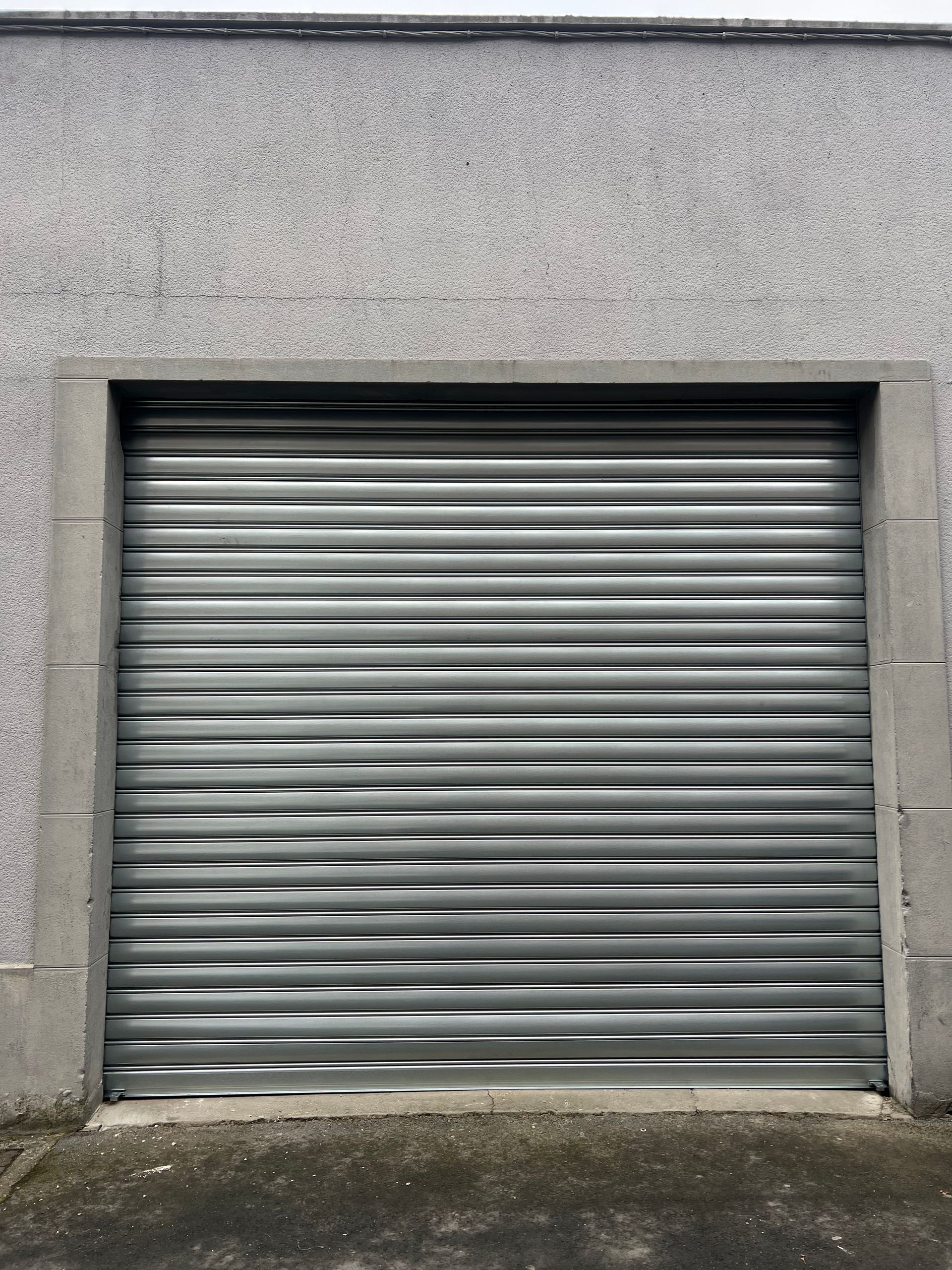 Porte sectionnelle argentée dans un cadre en béton gris sur un mur gris.