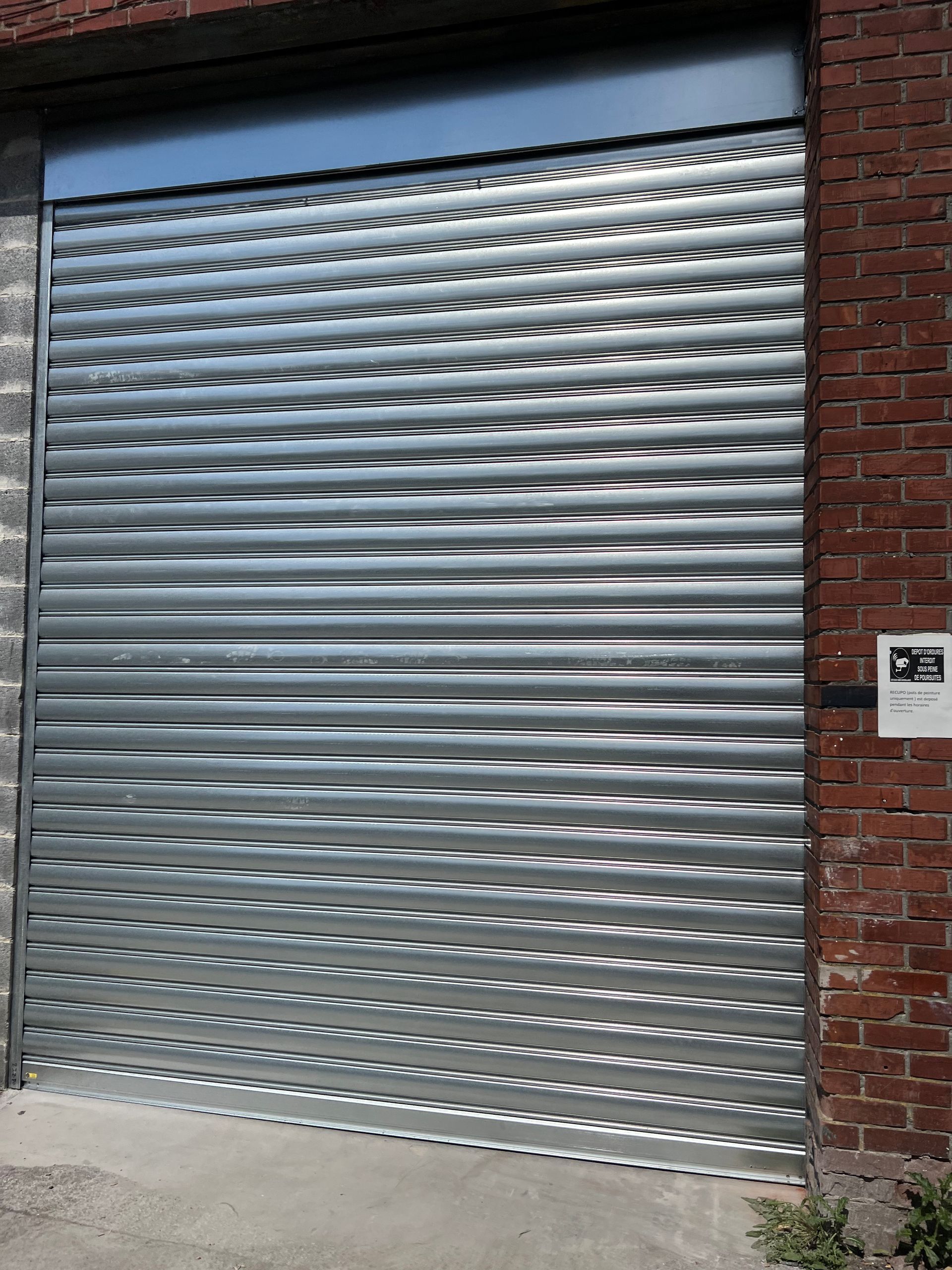 Porte de sécurité métallique à enroulement, partiellement fermée, installée dans un bâtiment en briques.