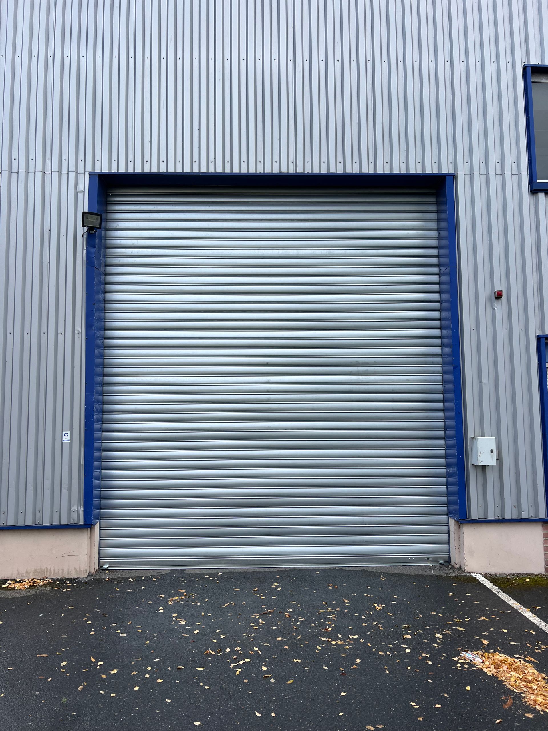 Porte sectionnelle métallique argentée sur un bâtiment avec bardage vertical argenté et garnitures bleues.