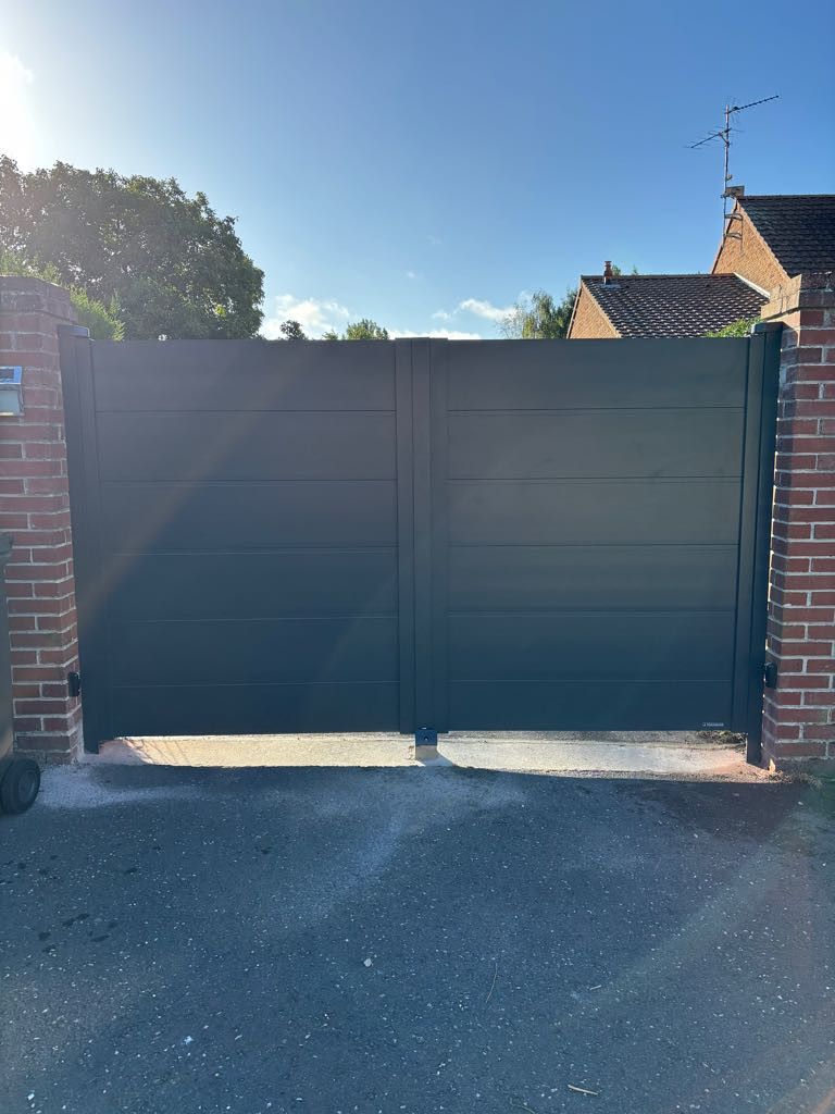 Portail d'allée en métal gris foncé entre des piliers en briques ; ciel bleu en arrière-plan.