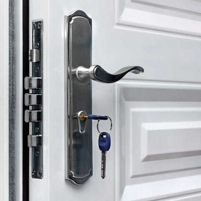 Poignée de porte argentée avec clé insérée, à côté d'une plaque de verrouillage assortie sur une porte blanche.