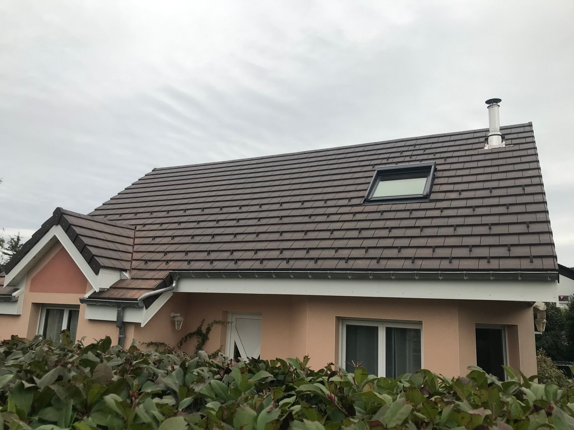 Un débord de toit gris foncé et un système de gouttières fixés au mur extérieur beige d'un bâtiment se détachant sur un ciel bleu clair.
