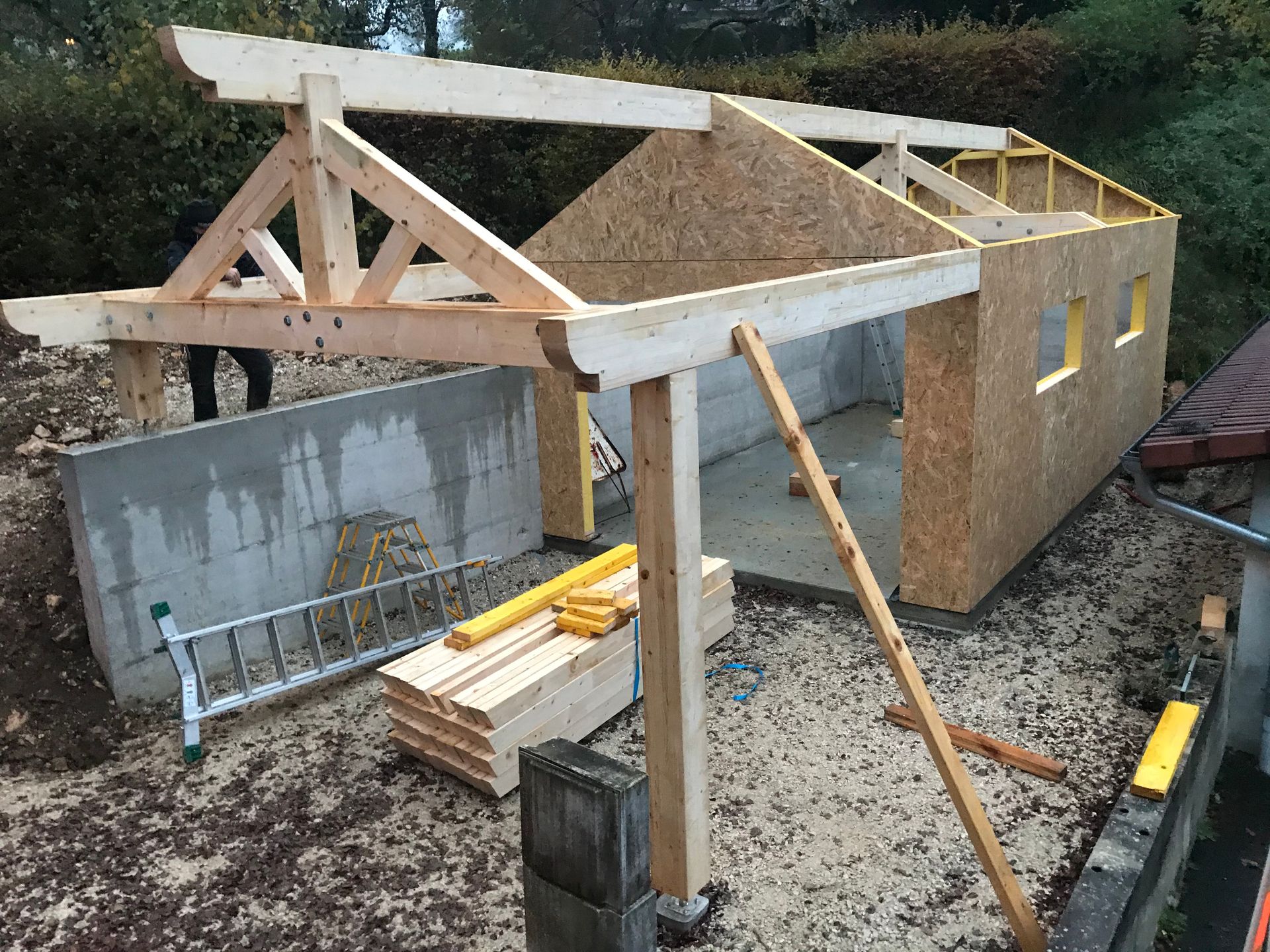 Une structure à ossature en bois pour un petit bâtiment en construction, comprenant une toiture à fermes et des panneaux de particules orientées.