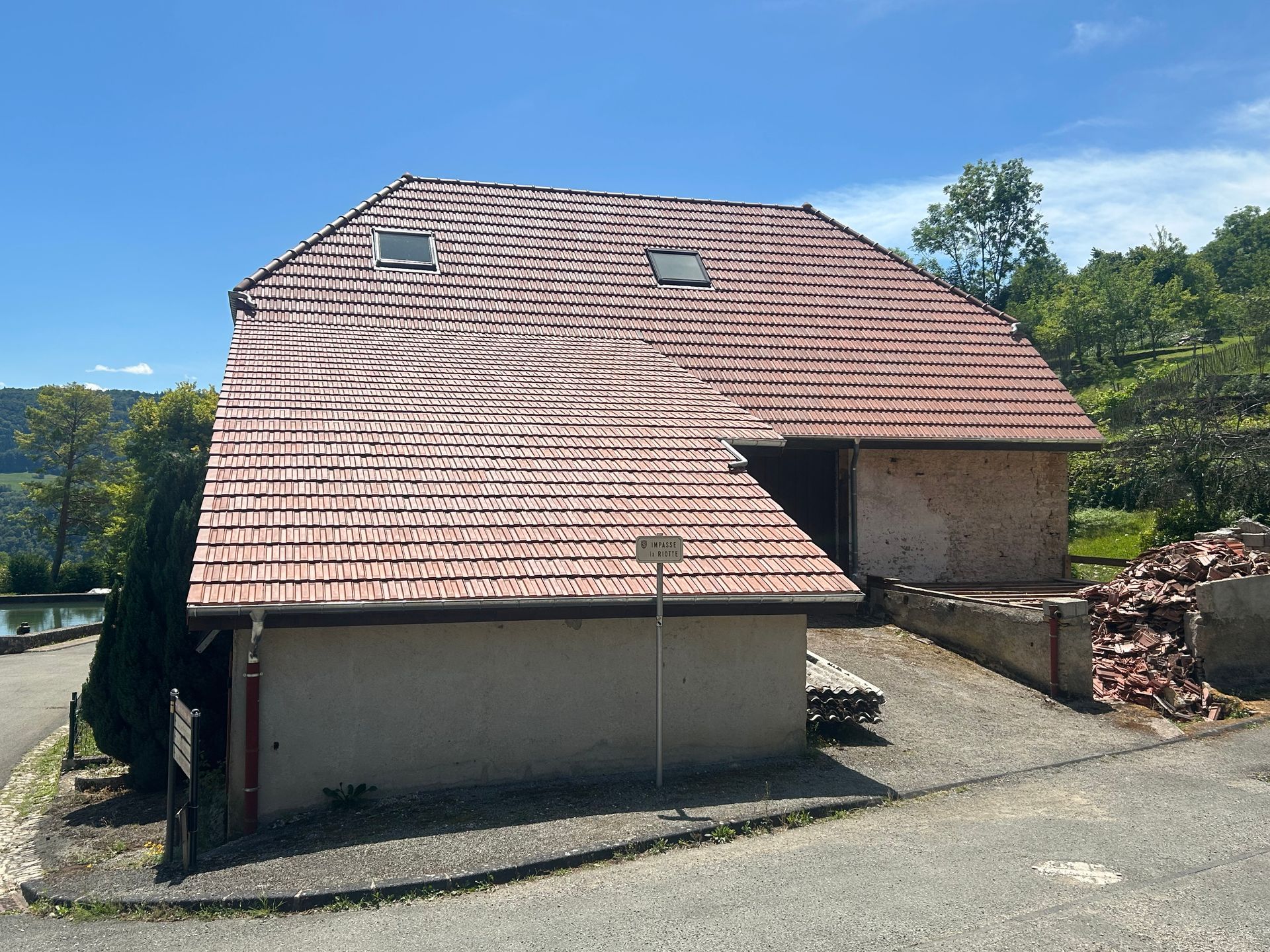 Vue latérale d'un bâtiment avec un toit à la texture déformée et ondulée, des murs en stuc beige et un tas de gravats sur la droite.