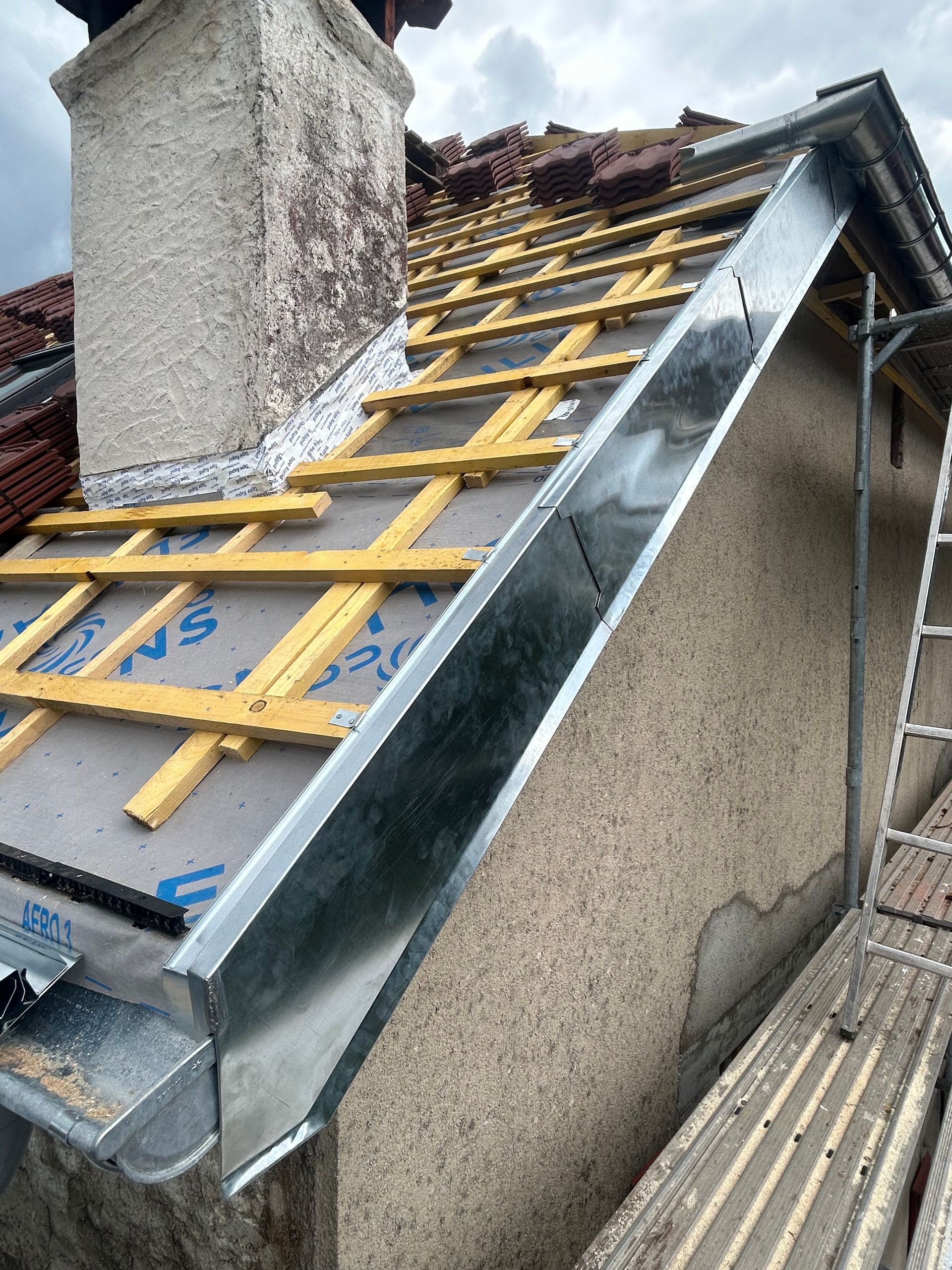 Vue en contre-plongée d'un coin de maison présentant un soffite de couleur claire, des gouttières en métal gris et une descente pluviale assortie.