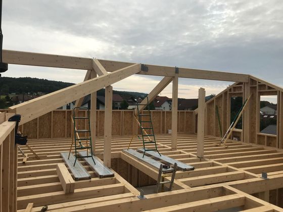 La charpente en bois d'une maison en construction, avec ses chevrons et ses solives apparents sous un ciel nuageux.