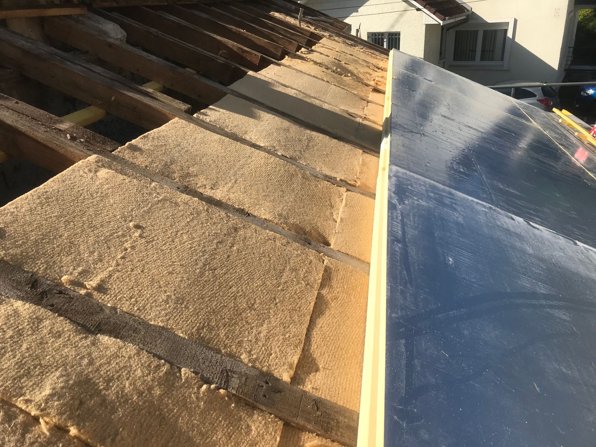 Toiture partiellement installée montrant des rangées de panneaux isolants entre les chevrons en bois, avec une section de panneaux solaires terminée.