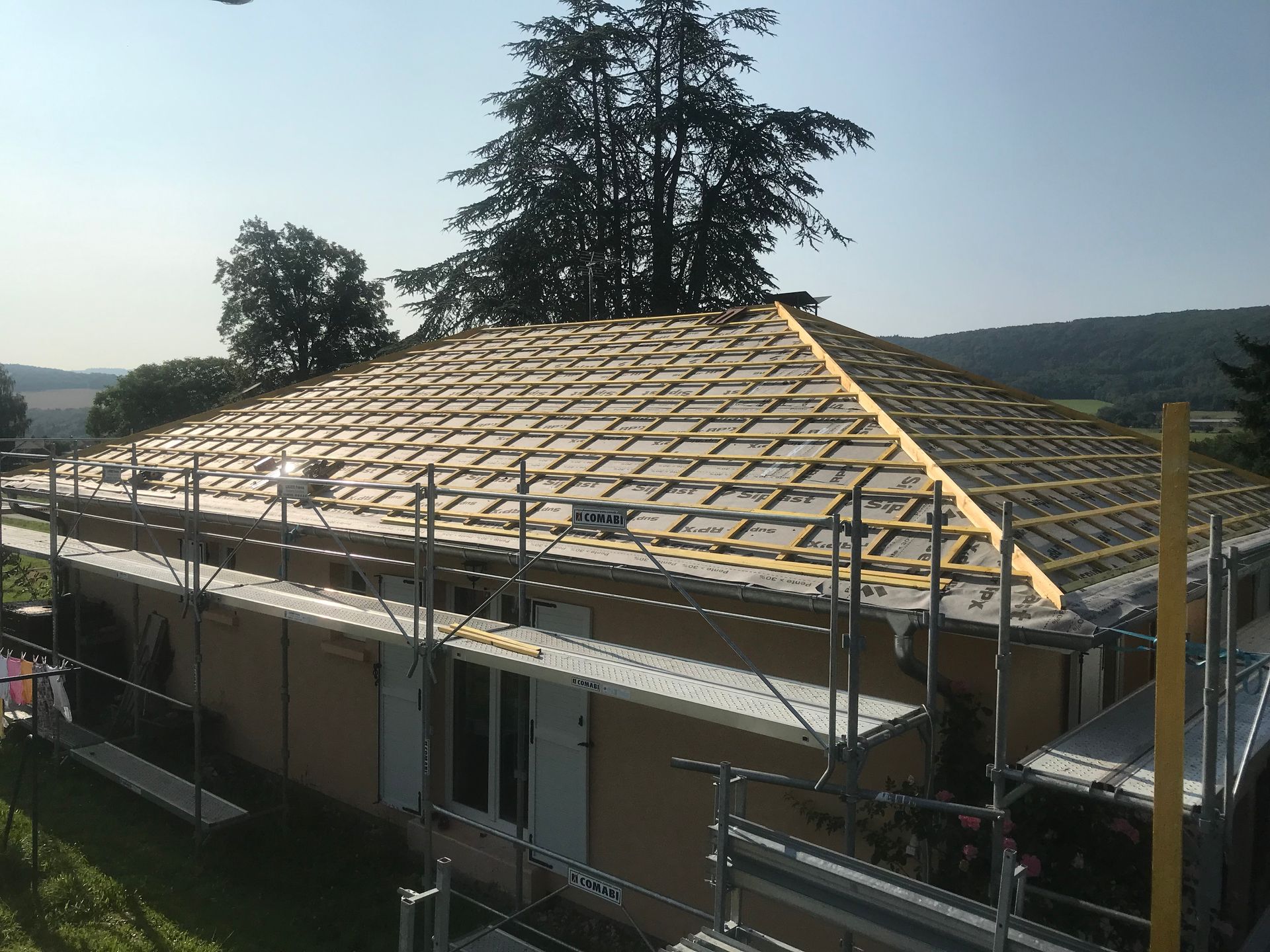 Une maison en construction, avec des échafaudages autour des murs et une nouvelle charpente de toit en bois installée.