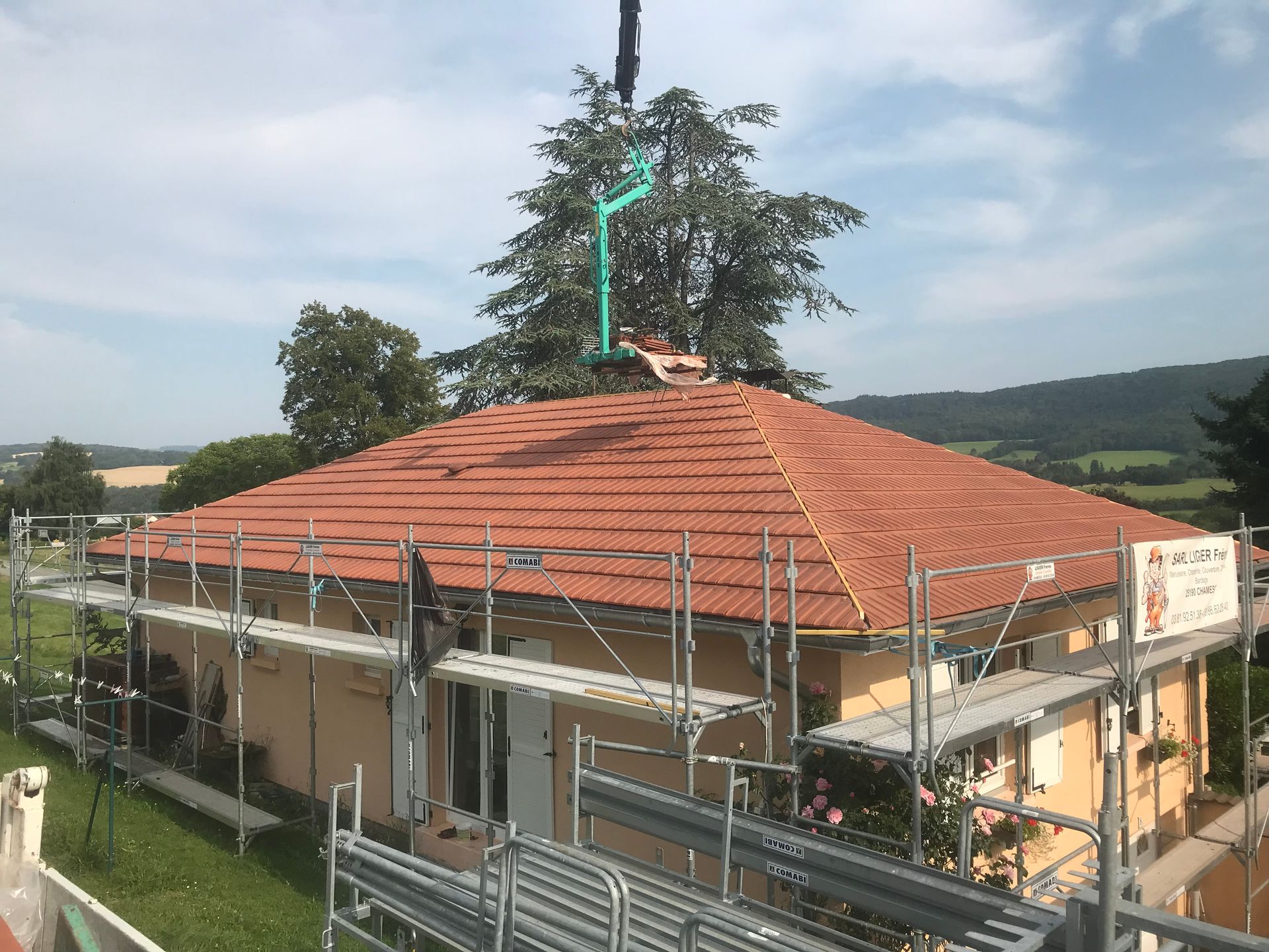 Une maison avec un toit à quatre pans récemment recouvert de tuiles, entourée d'échafaudages métalliques, vue d'un point de vue surélevé.