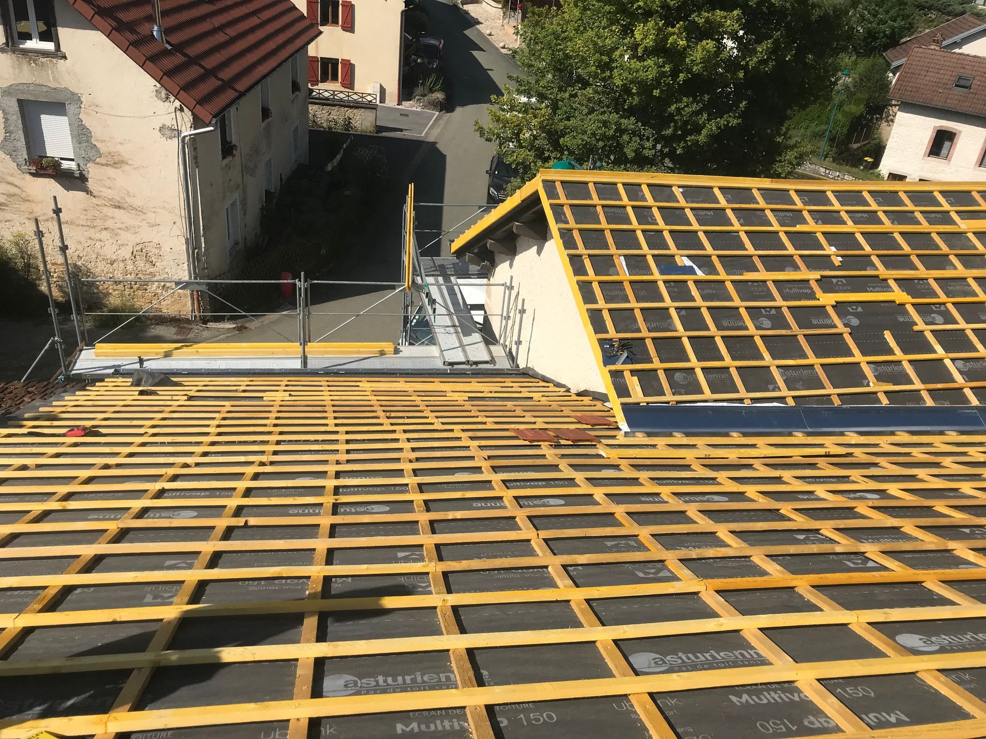 Un toit en construction avec une grille de liteaux en bois jaune installée sur un feutre de toiture noir.
