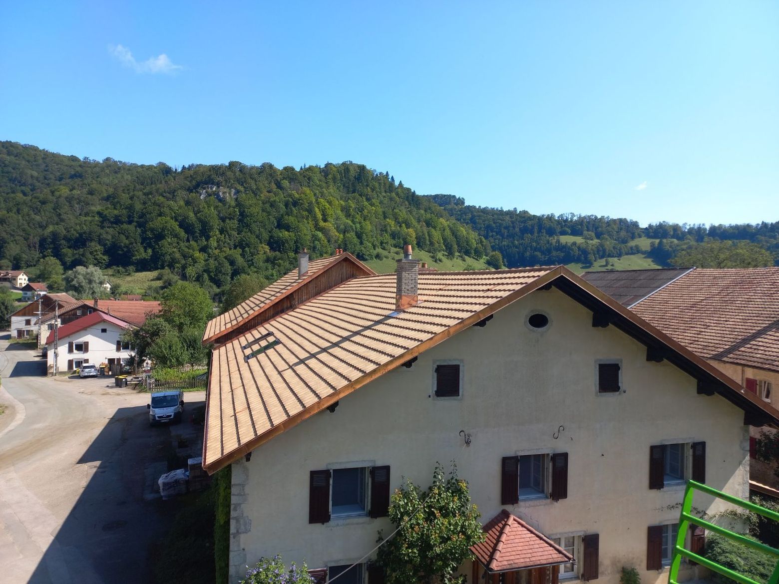 Vue aérienne d'une maison couleur sable avec un toit de tuiles neuves, se détachant sur un fond de colline verdoyante et de route.