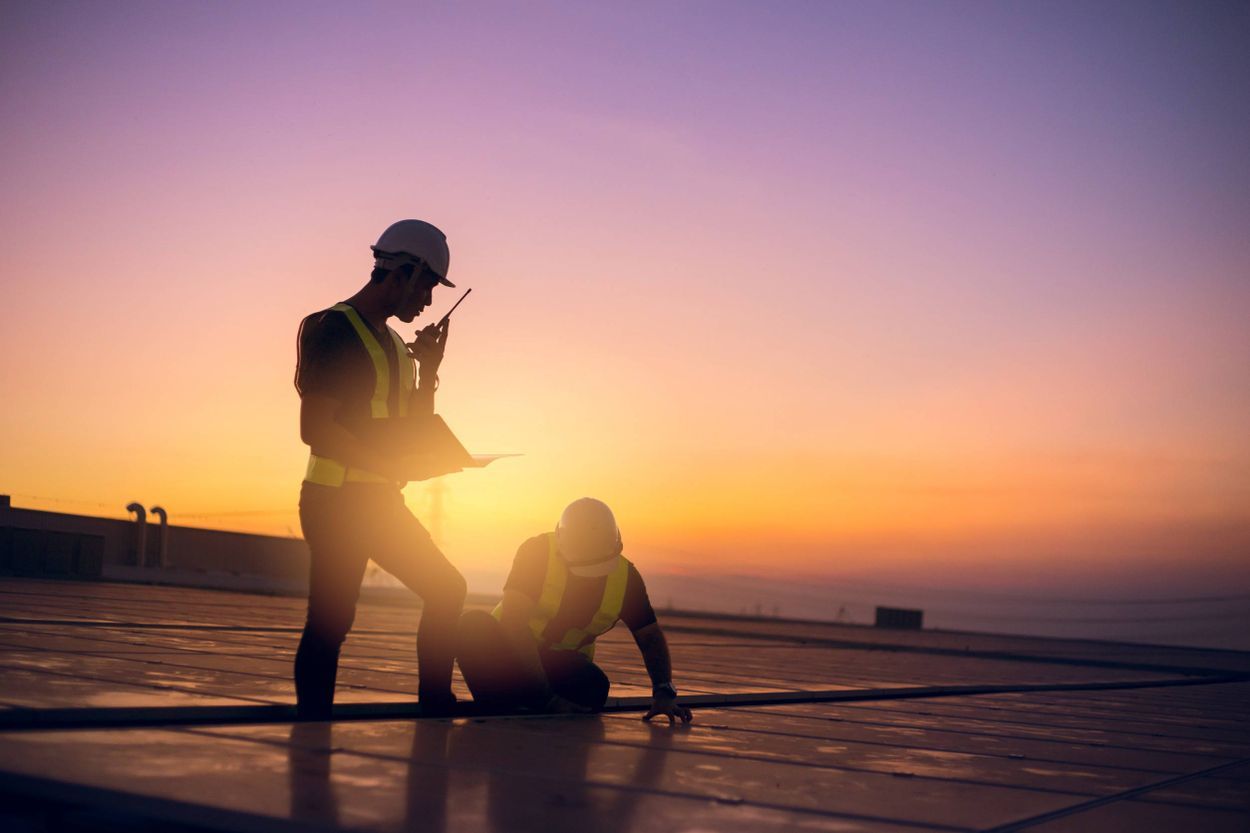 Dos obreros de la construcción trabajan en un tejado al atardecer.