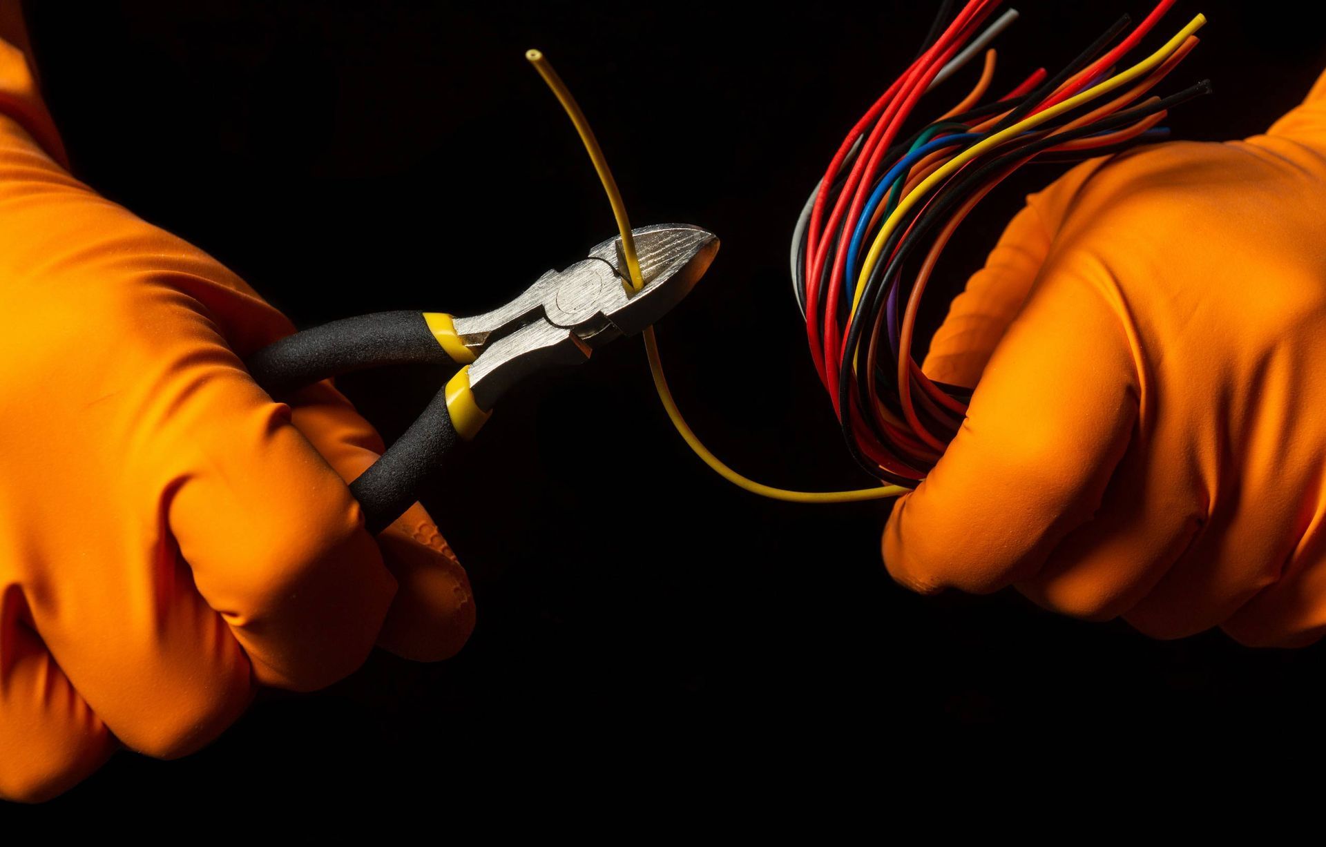Una persona que lleva guantes naranjas sostiene un par de alicates y un montón de cables.