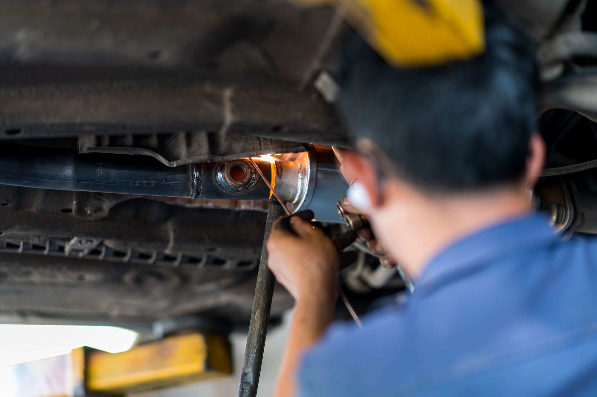 Un hombre está soldando un tubo debajo de un coche en un garaje.