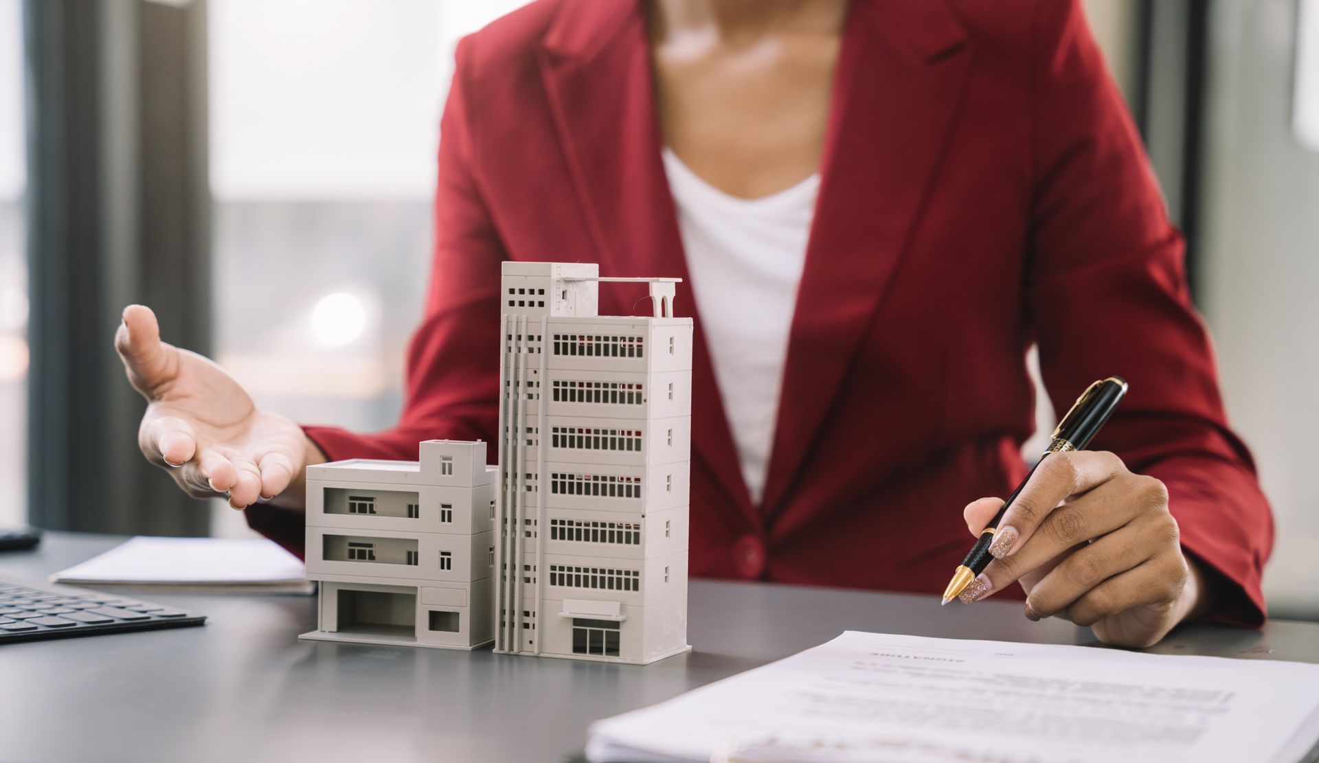 Photo d'une femme avec un stylo à la main assise à un bureau devant la maquette d'un immeuble et un contrat