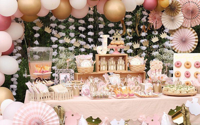 Una mesa decorada para una fiesta de cumpleaños con globos, abanicos y flores.