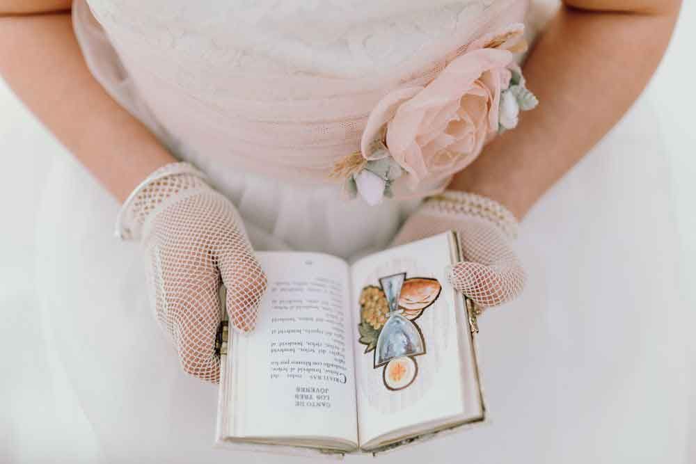 Una mujer con un vestido blanco sostiene un libro en sus manos.