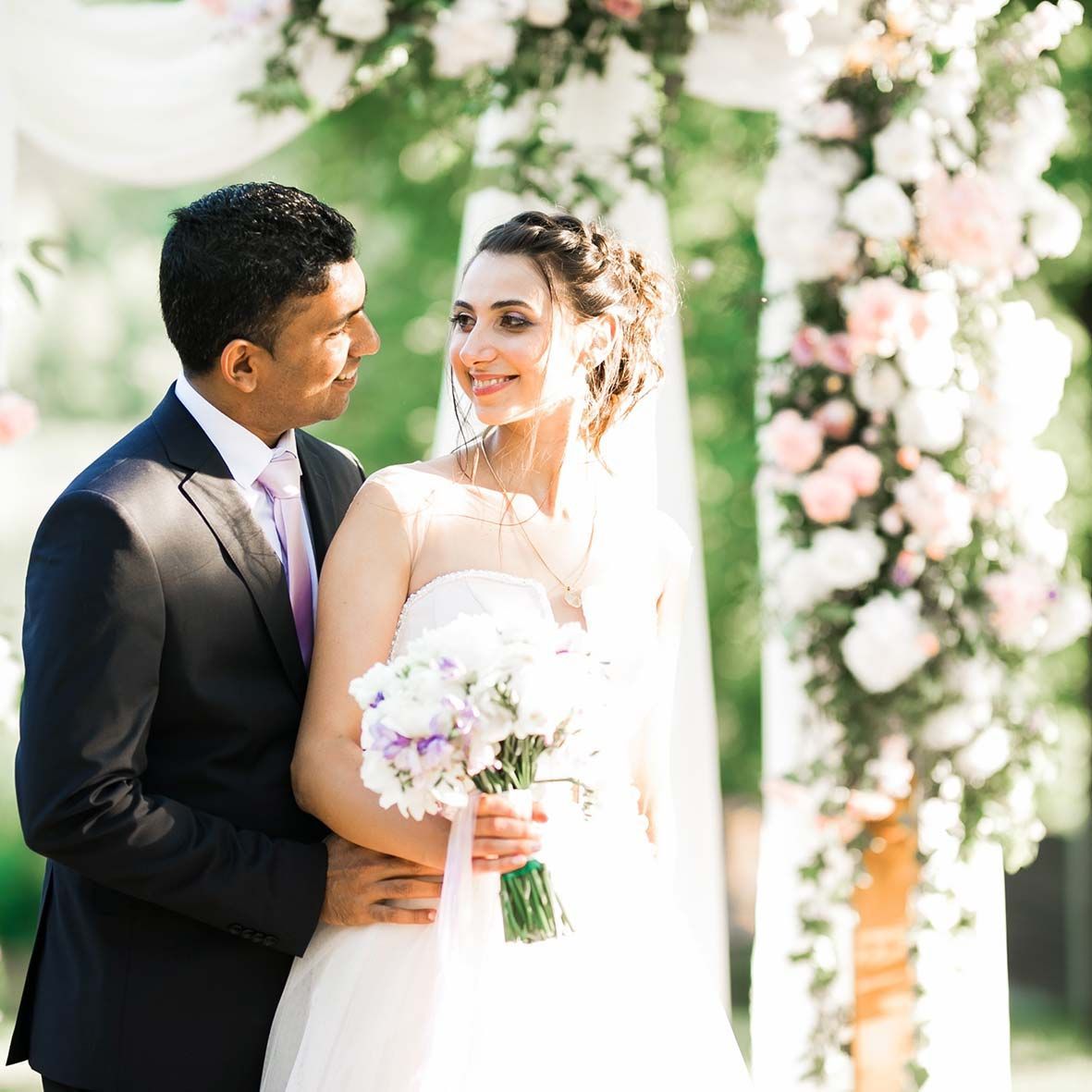 Una novia y un novio posan para una fotografía delante de un arco floral.