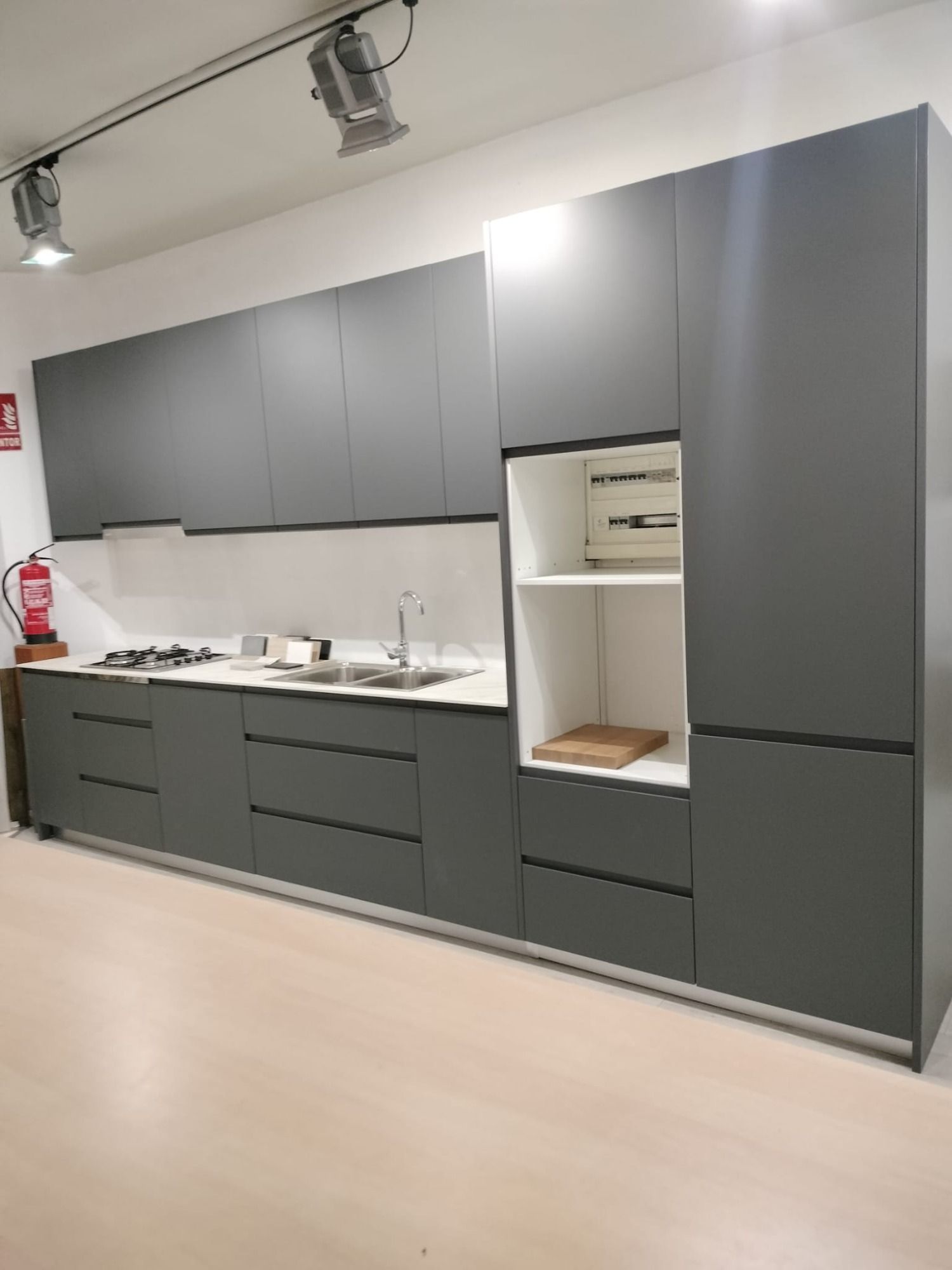 Muebles de cocina modernos de color gris con salpicadero blanco y estanterías integradas en una sala de exposición.