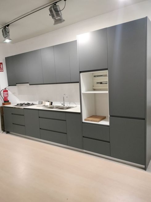 Muebles de cocina modernos de color gris con salpicadero blanco y estanterías integradas en una sala de exposición.