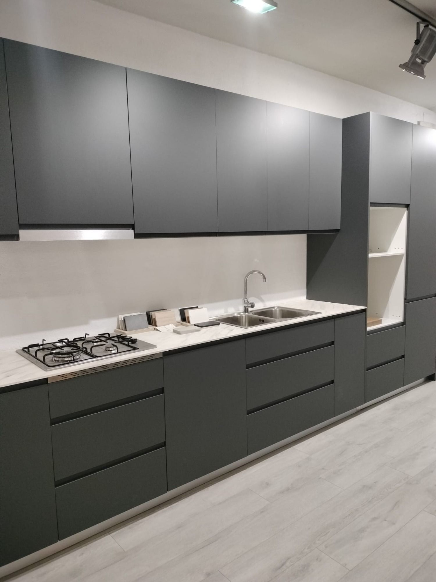Cocina moderna con gabinetes gris oscuro, encimera blanca, fregadero, estufa y estantes abiertos.