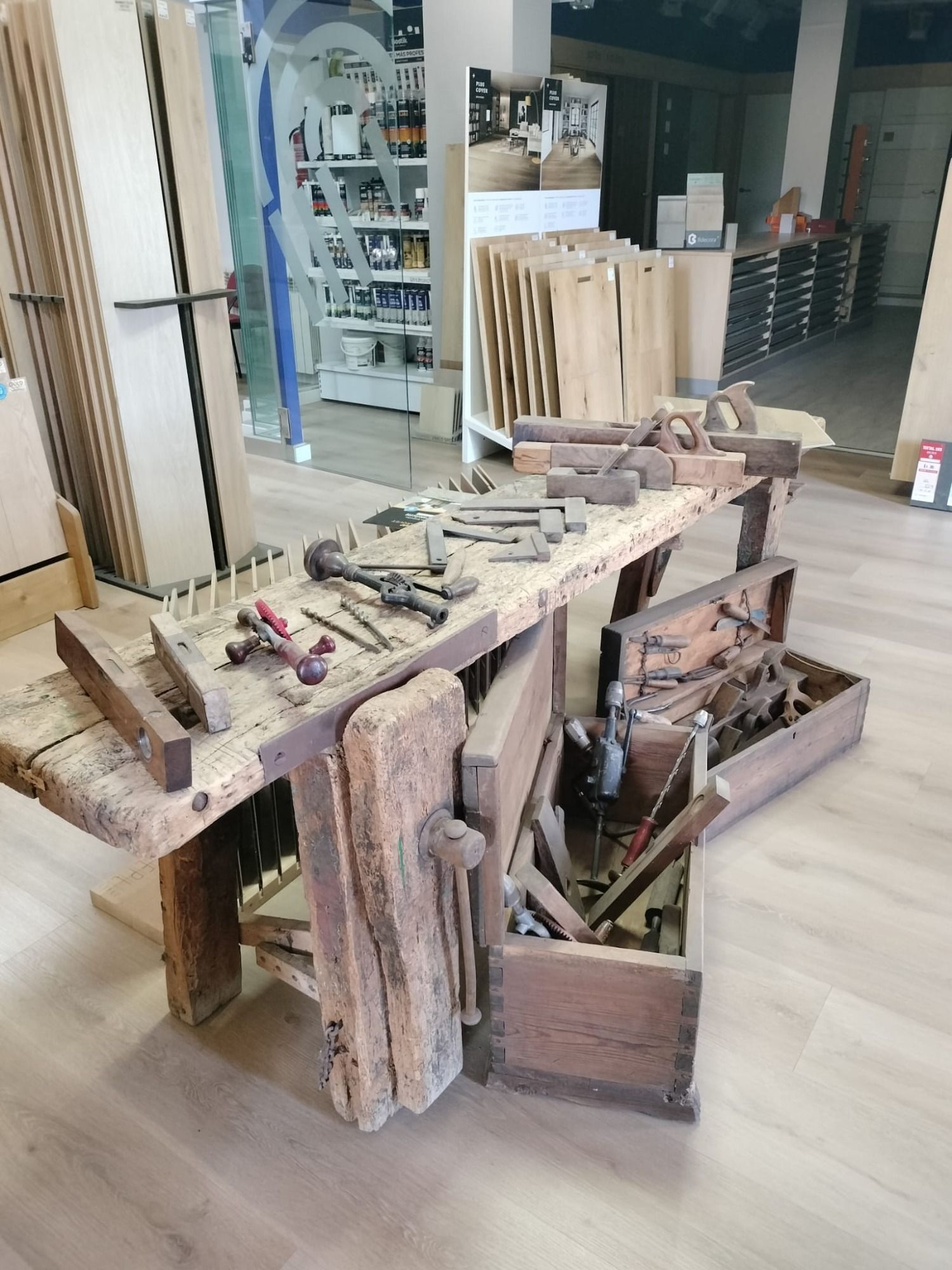 Banco de trabajo rústico de madera con herramientas y restos de madera en una sala de exposición de un taller.