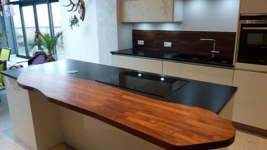 Cuisine moderne avec un plan de travail noir et un grand îlot en marbre effet bois au premier plan.