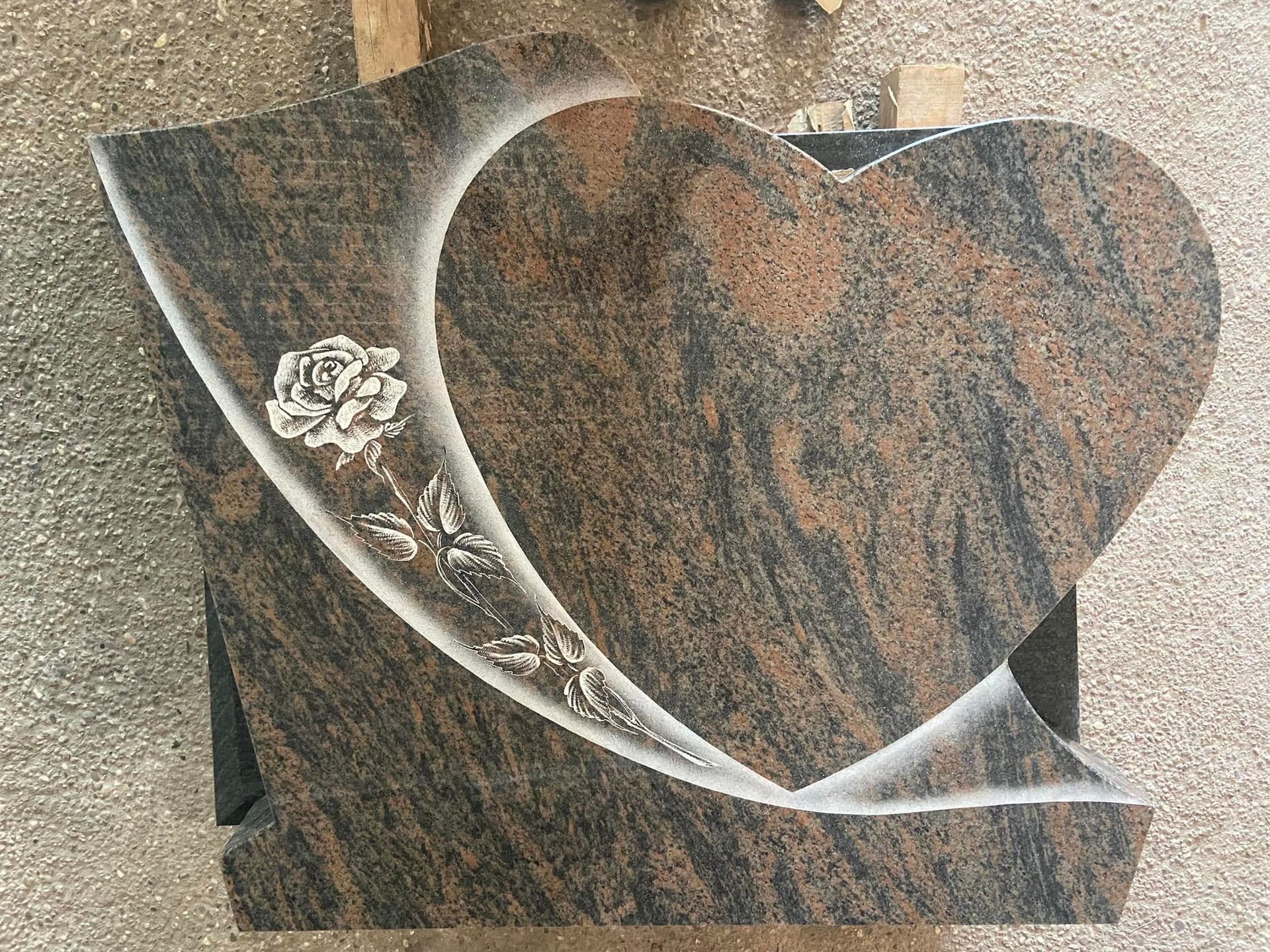 Plaque commémorative en granit en forme de cœur avec une rose blanche gravée sur un socle en pierre sombre.