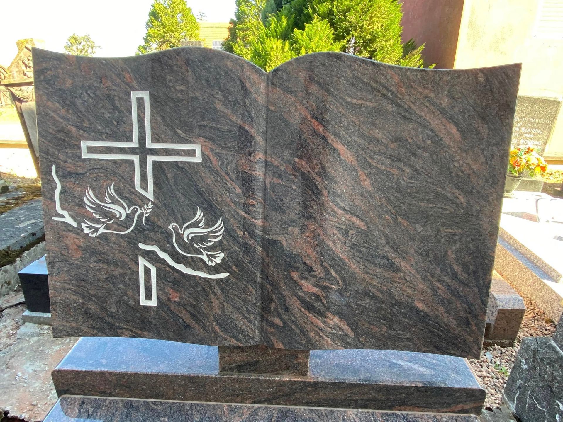 Pierre tombale commémorative en granit sombre ornée de gravures de croix et de colombes, dans un cimetière en plein air.