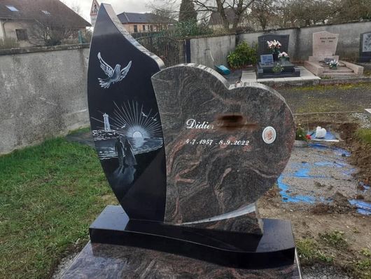 Pierre tombale noire et grise en forme de cœur ornée de colombes et de bougies dans un cimetière