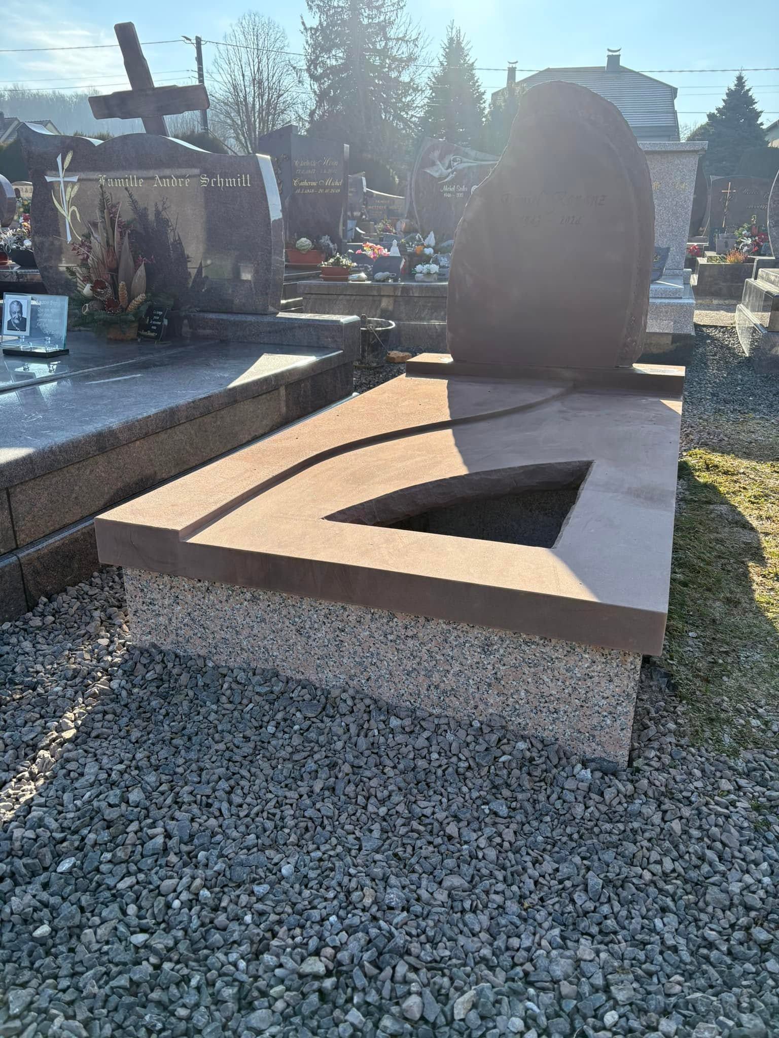 Tombe avec un monument funéraire en granit incliné et un insert noir, sur une parcelle de cimetière recouverte de gravier.