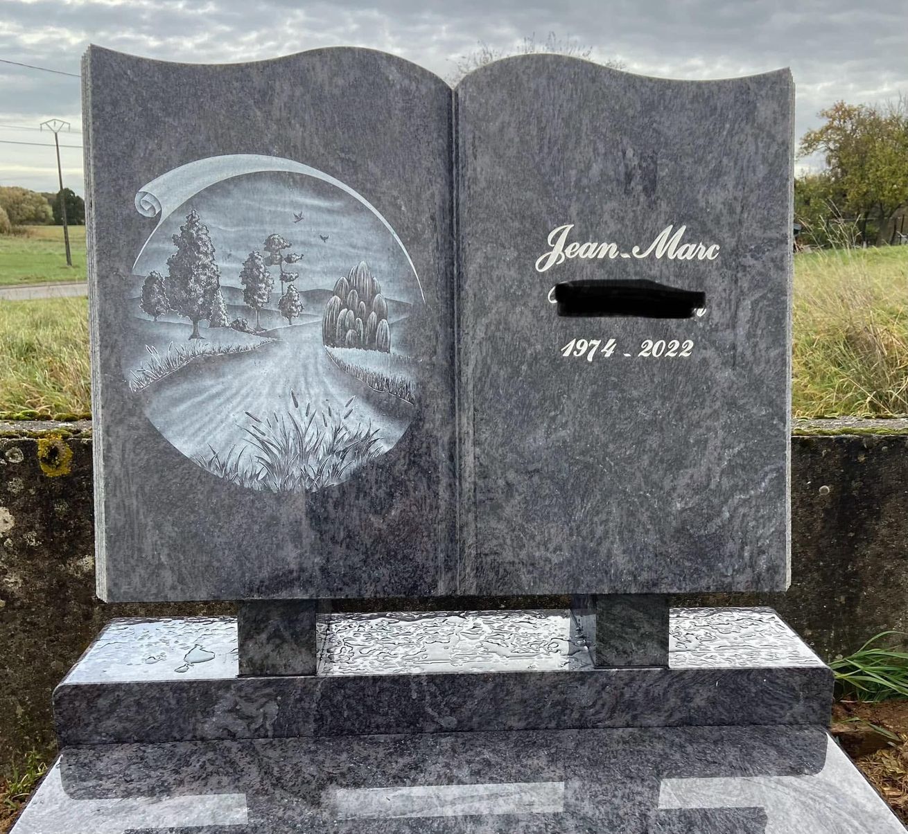 Pierre tombale en granit avec une gravure ronde représentant un paysage d'hiver.