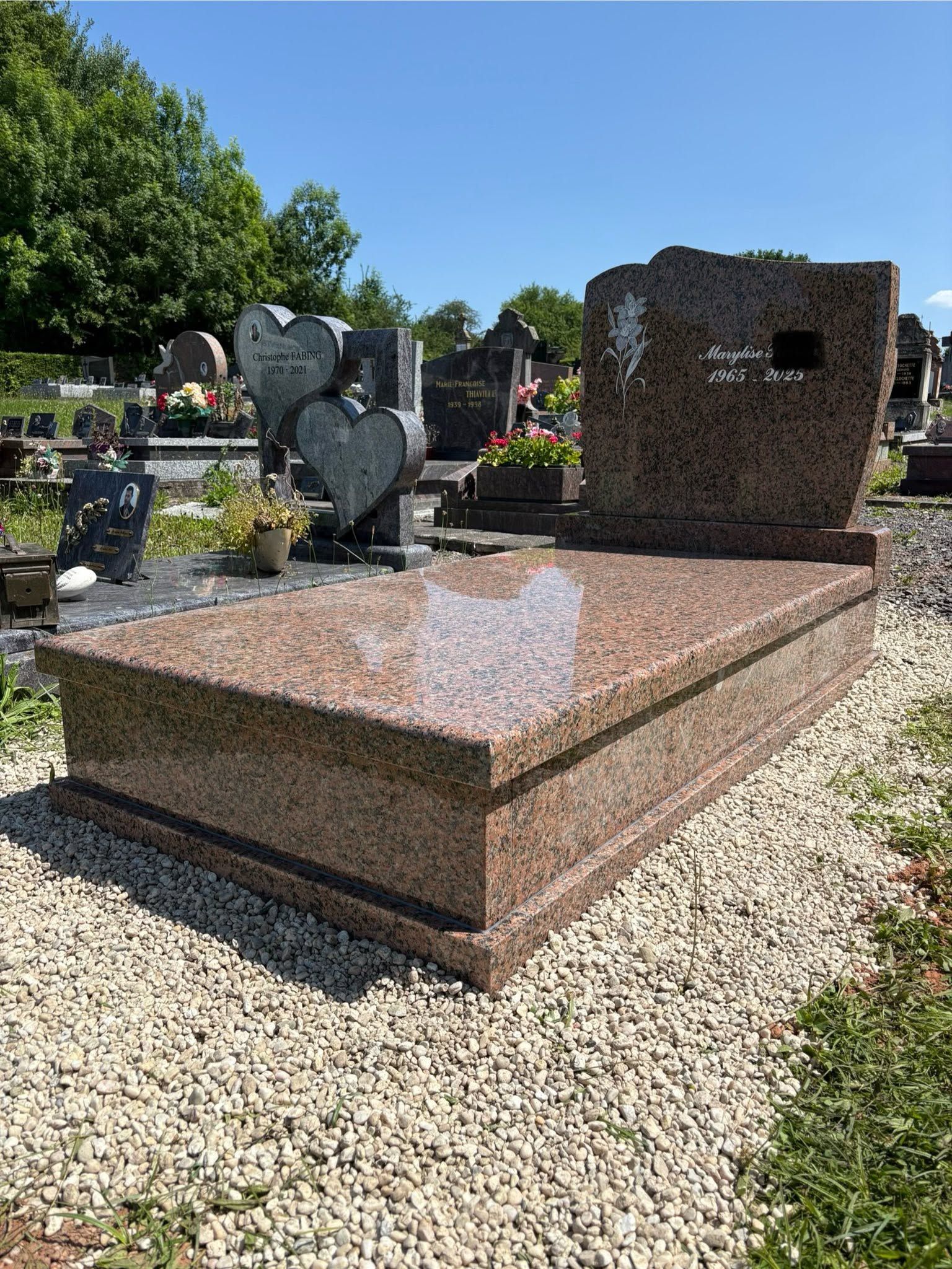 Monument funéraire en granit avec socle rose poli et stèle verticale sombre dans un cimetière.