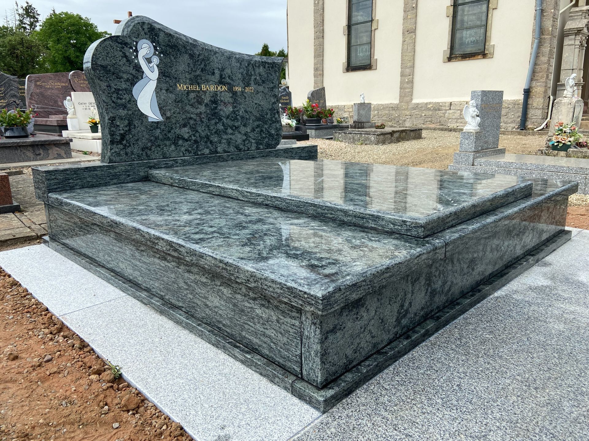 Monument funéraire en granit poli orné de gravures florales blanches, dans un cimetière.