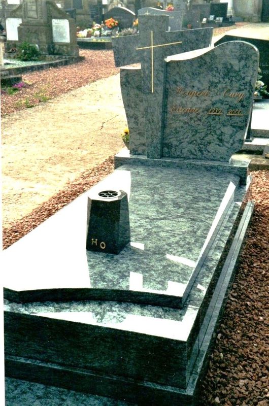 Pierre tombale en granit avec une stèle incurvée dans un cimetière, entourée de gravier et d'autres pierres tombales.