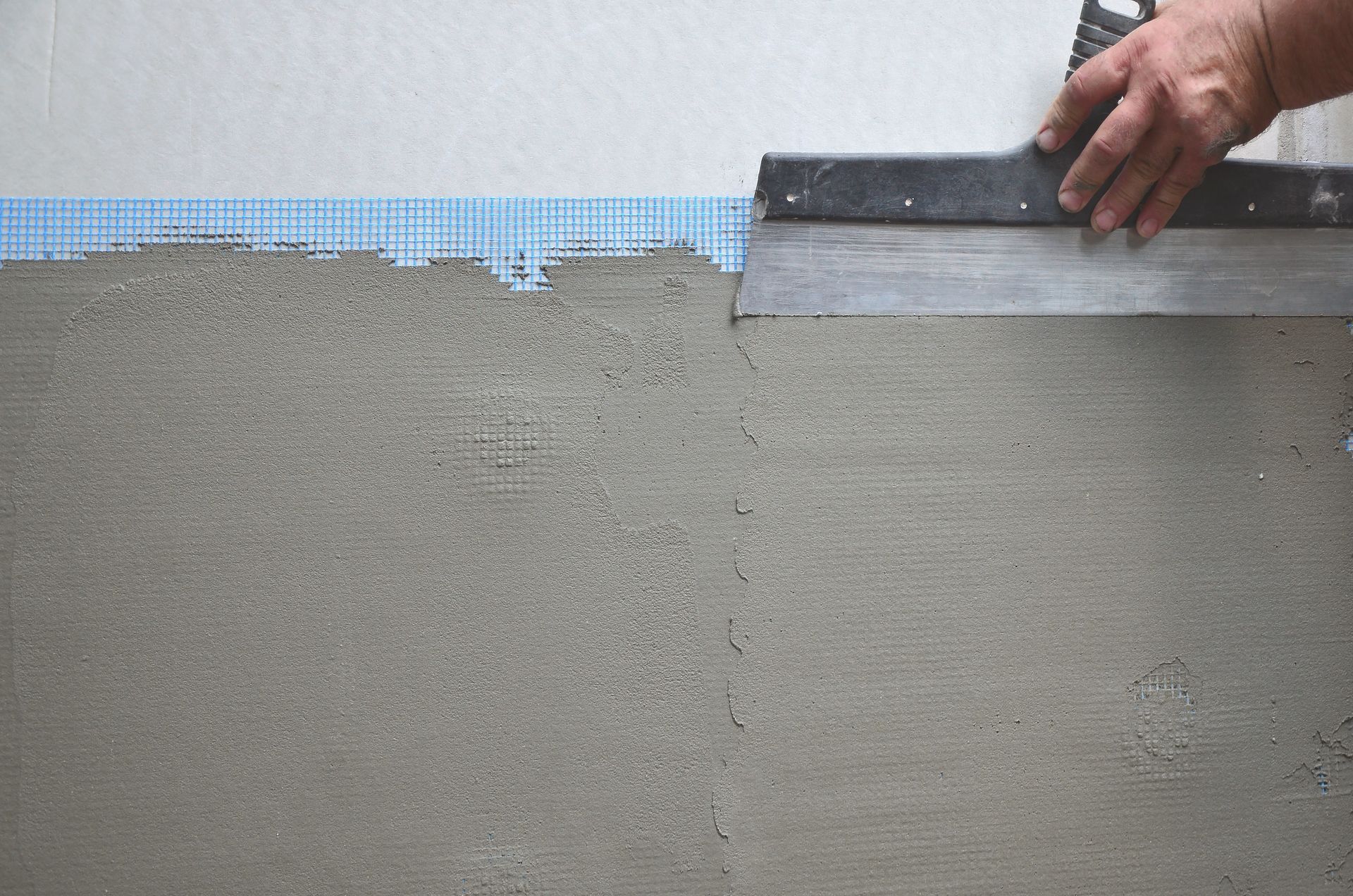 Zoom sur la mains d'un homme posant de l'enduit