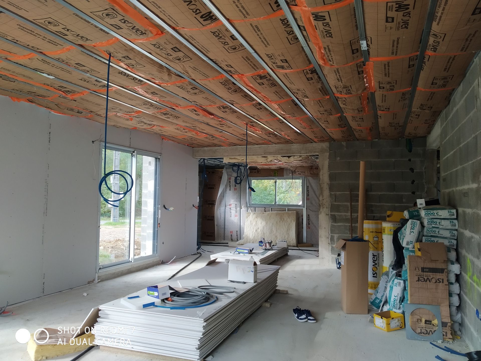 Intérieur d'une maison en construction ; les cloisons sèches et les matériaux sont visibles dans la pièce.