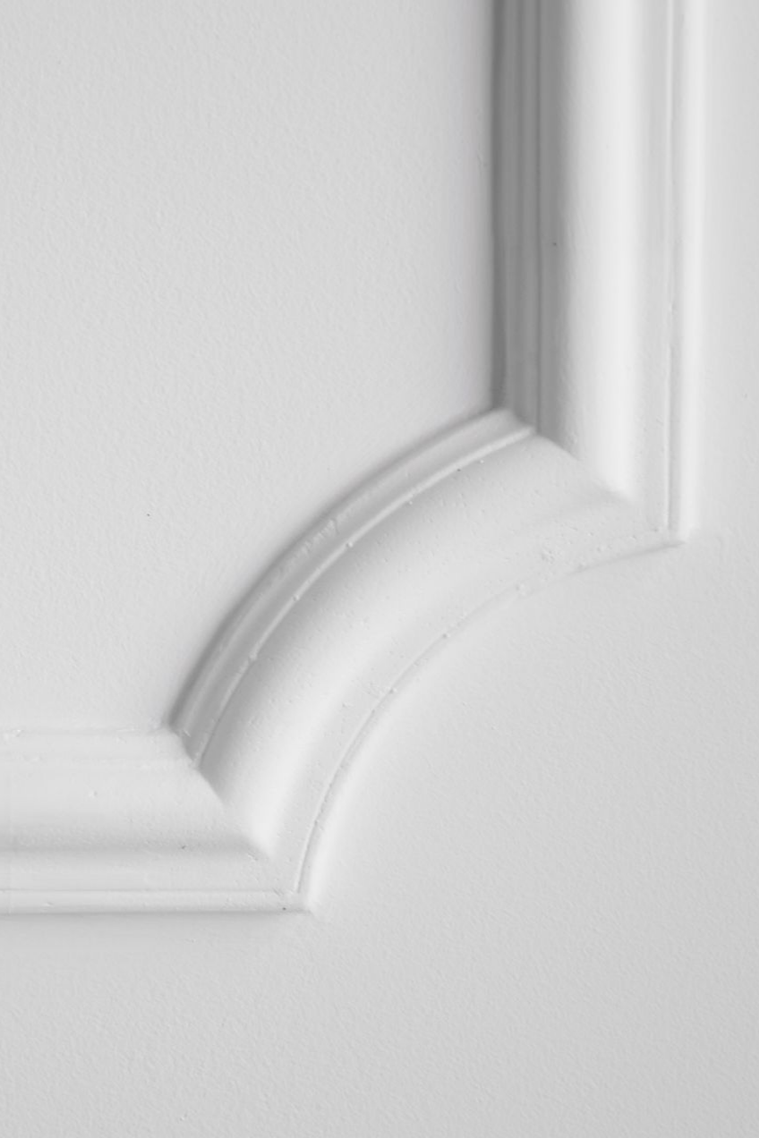 Gros plan sur une moulure de corniche blanche à détails incurvés, dans un coin de mur.