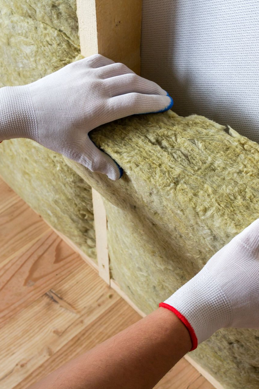 Mains gantées, installant l'isolant entre les montants muraux en bois.