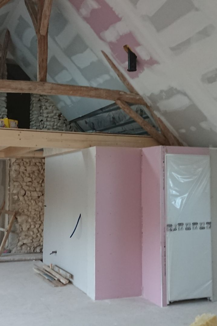 Intérieur d'un grenier en rénovation, avec poutres apparentes, isolation rose et cloisons sèches.