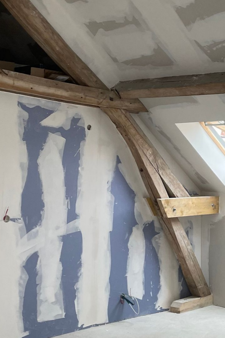 Rénovation intérieure en cours, montrant les poutres en bois apparentes et les cloisons sèches.