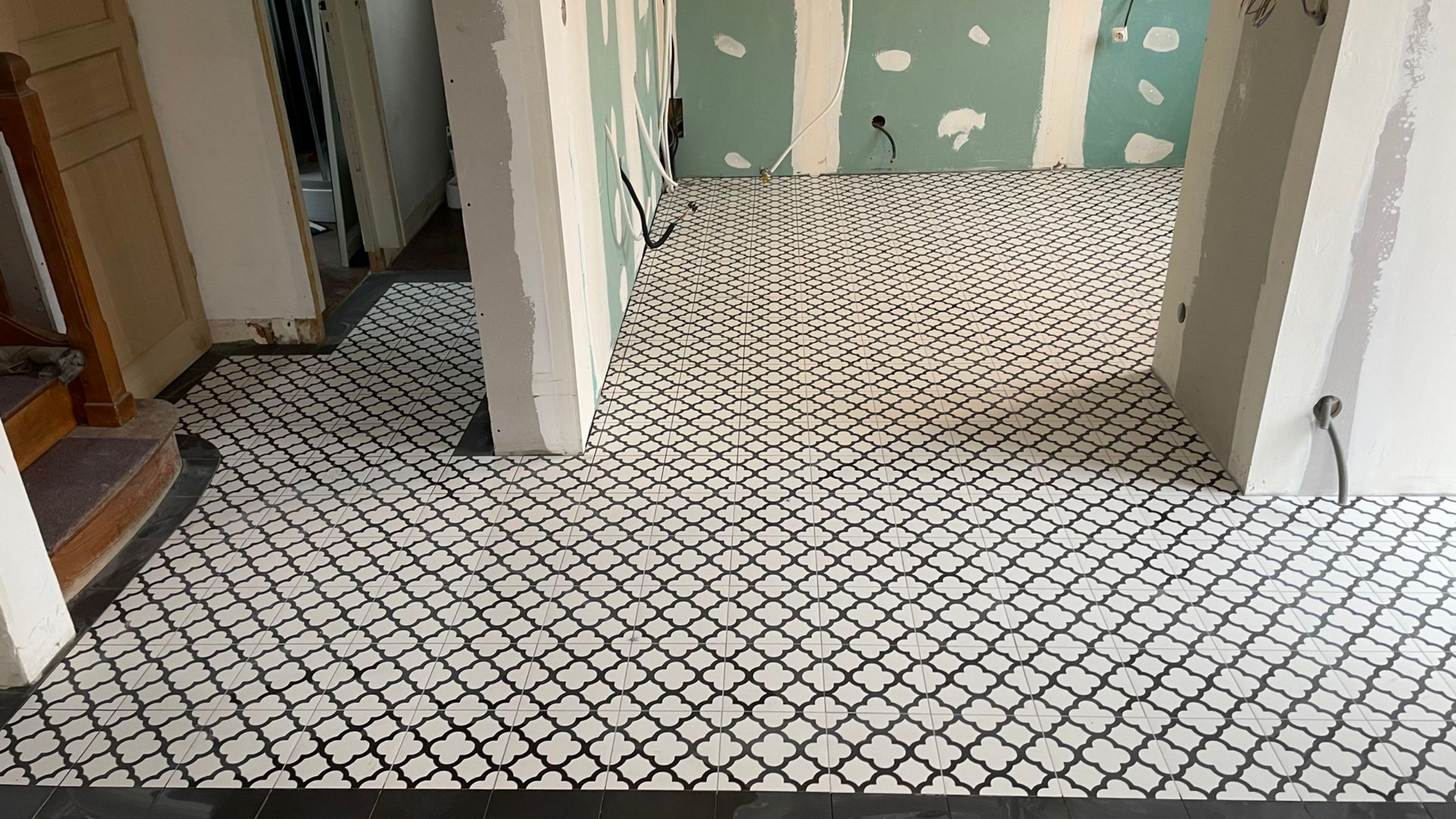 Carrelage à motifs noirs et blancs au sol dans une pièce en construction, avec cloisons sèches et poutres de soutien apparentes.