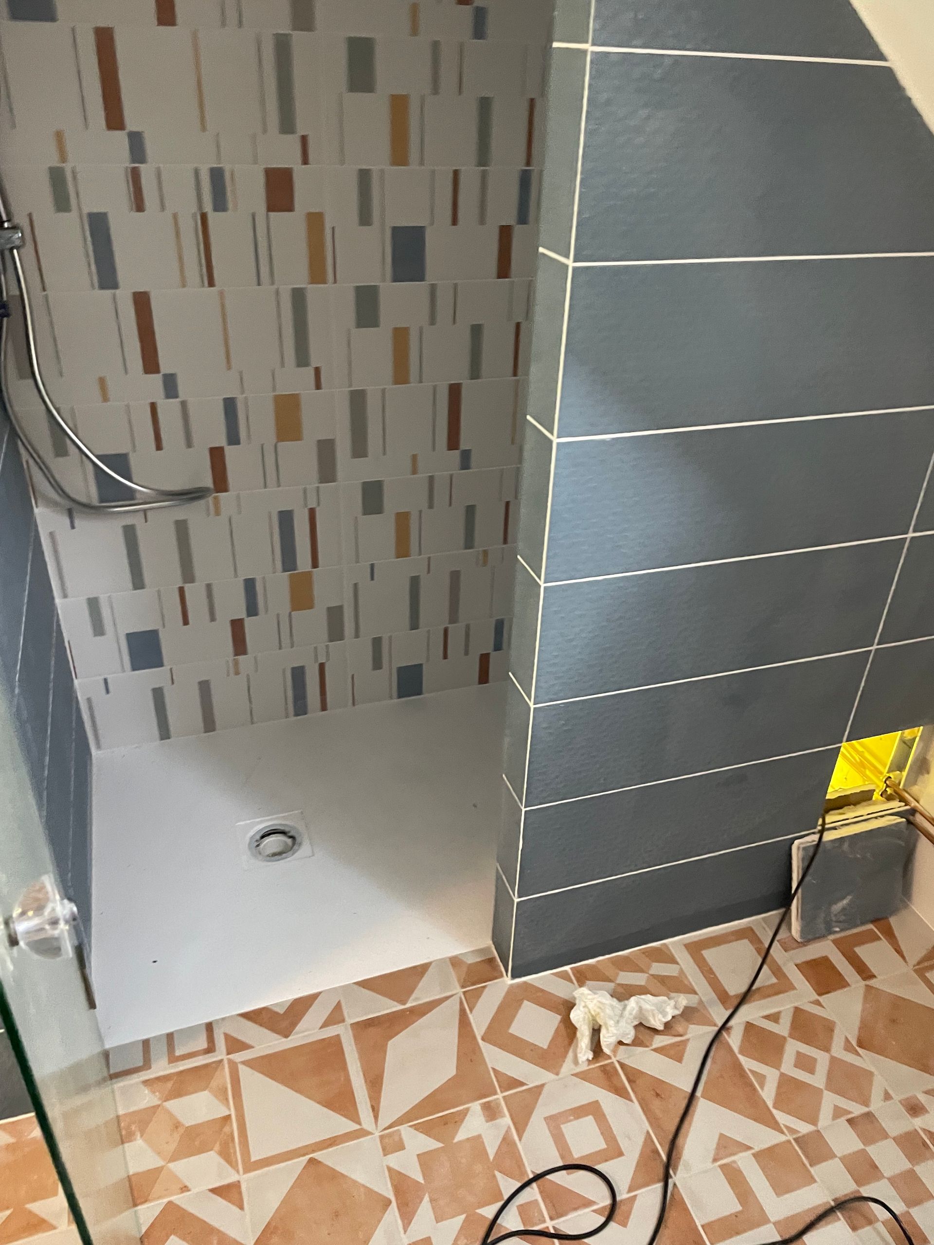 Douche avec receveur blanc, carrelage à motifs et mur d'accent bleu. Carrelage au sol marron et orange.
