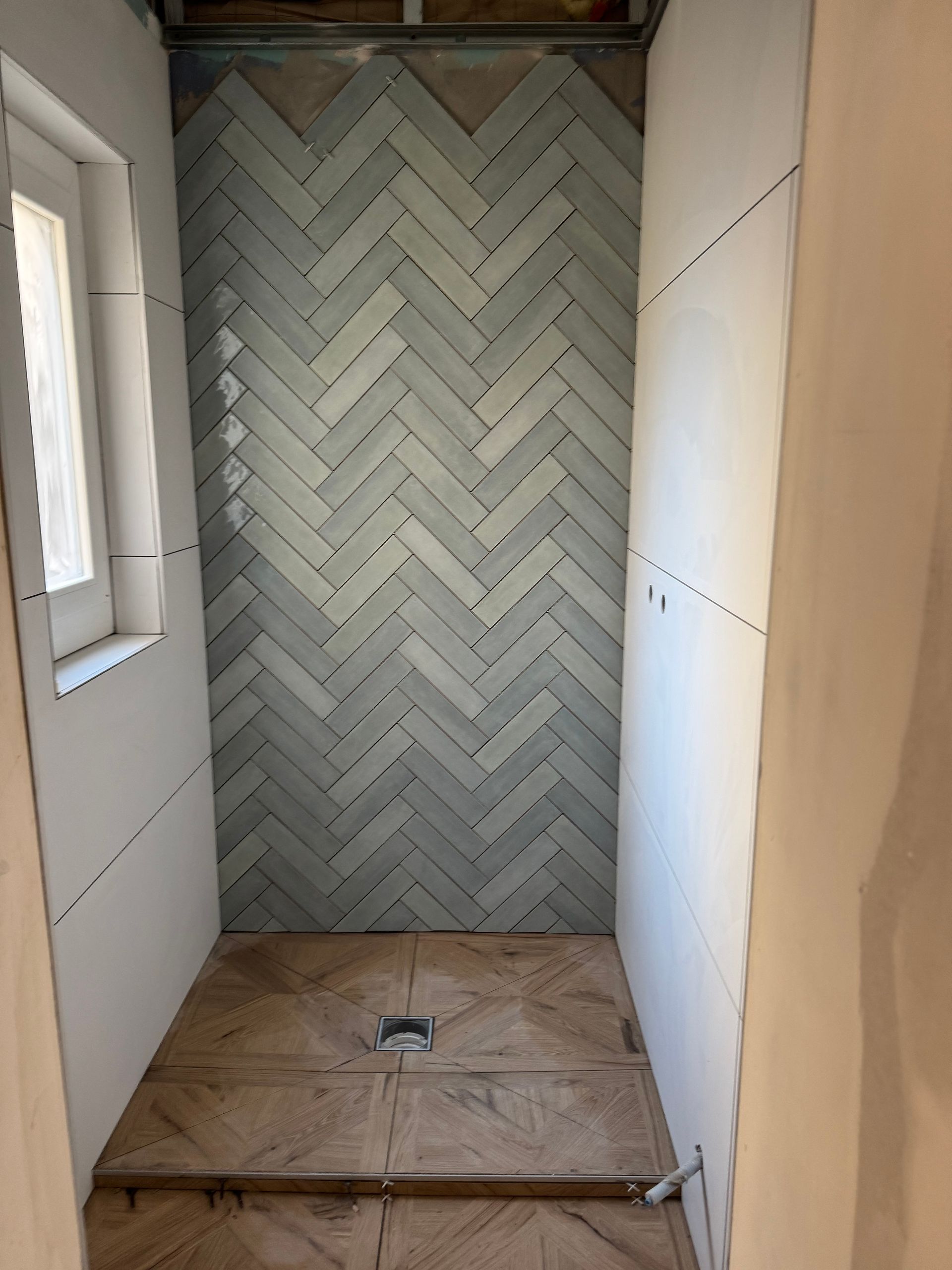 Cabine de douche avec mur carrelé à chevrons, murs non finis et sol en bois.