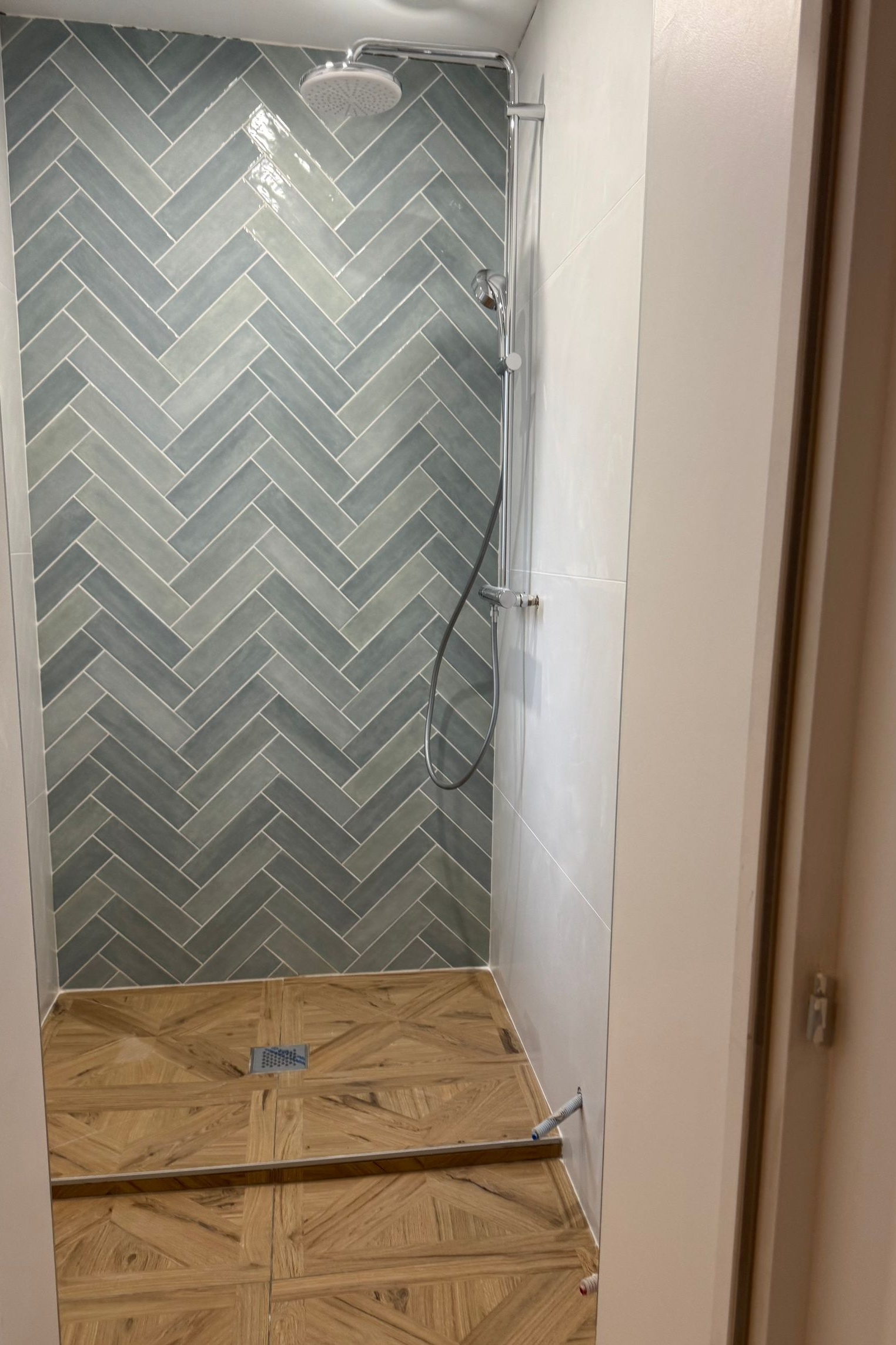 Cabine de douche avec mur carrelé de carreaux bleus à chevrons et sol imitation bois. Robinetterie chromée.